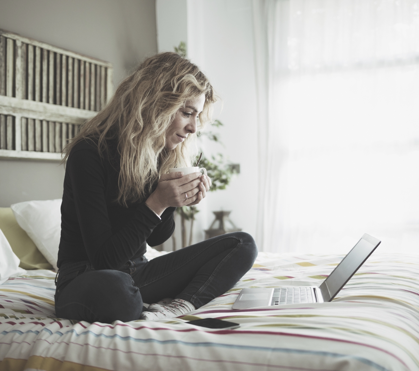 woman sitting in bed with coffee and a laptop